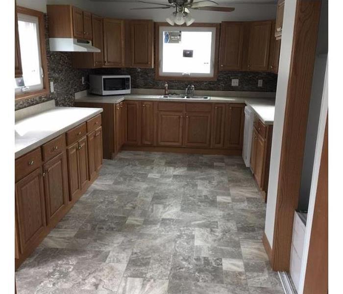 The damaged kitchen is remodeled with appliances and cabinets.