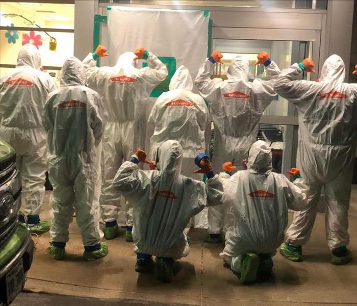 image of 8 servpro cleaning technicians turned around pointing to the back logo of their ppe suits