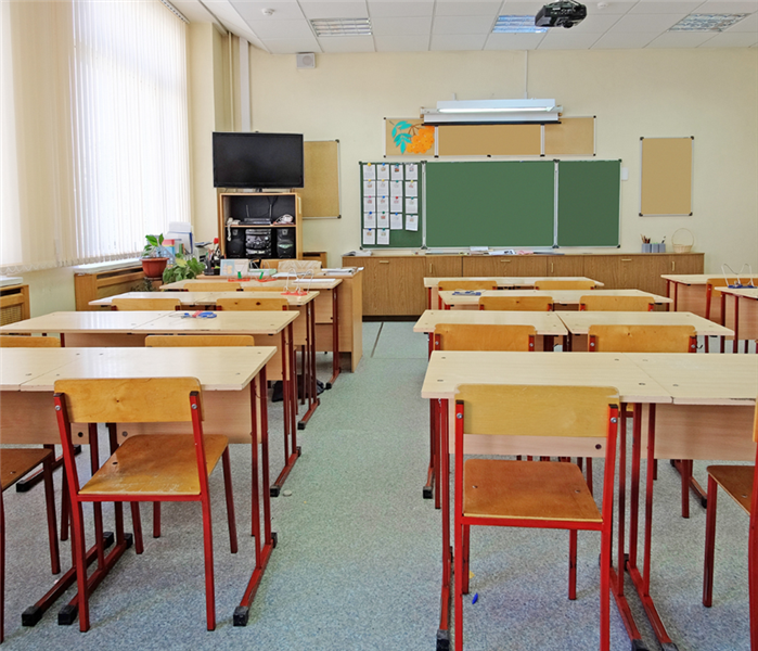 Picture is of a empty classroomwith wooden desks and a green chalk board in the background. 